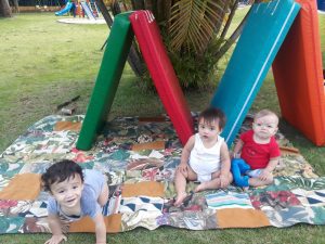 Bebês brincando de cabana com colchonetes e bambolês.