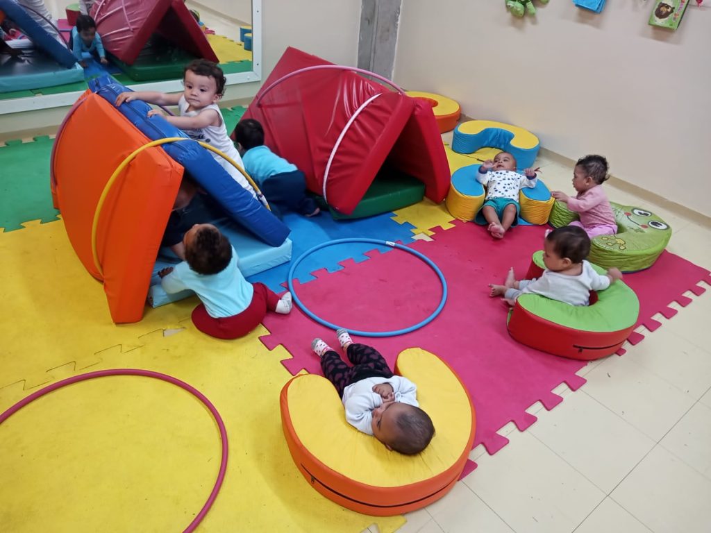 Bebês brincando de cabana com colchonetes e bambolês.